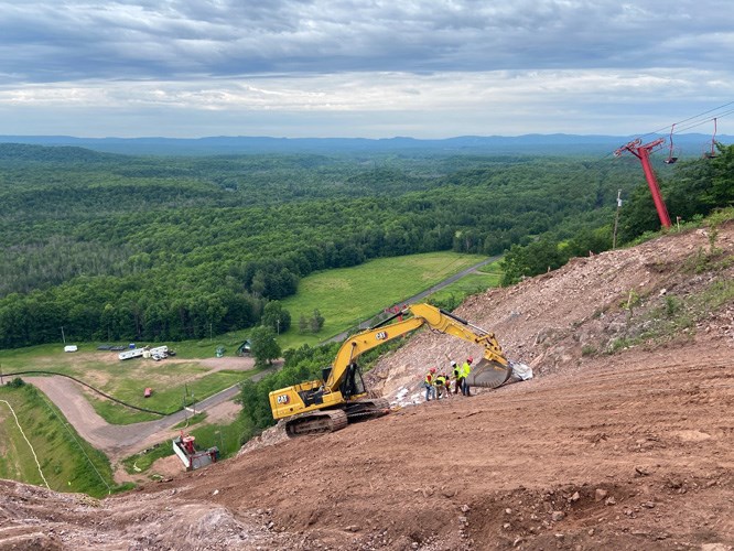 An excavator and construction workers shaping a ski jump landing hill.