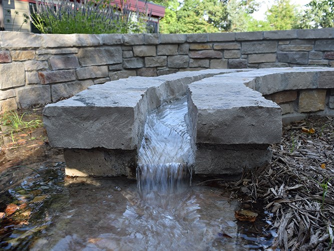 A spiral-shaped wall with a narrow channel on top conveying running stormwater into a raingarden.
