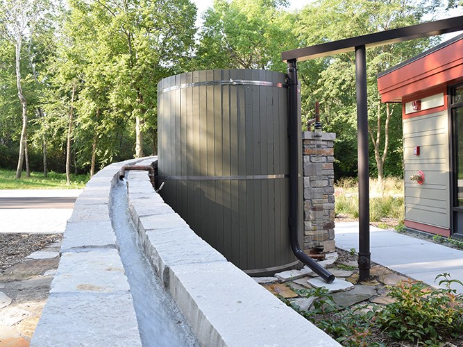 A modern building with large glass windows and a flat red roof surrounded by planted grasses.