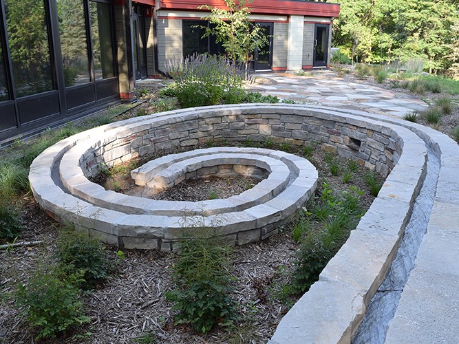 A modern building with large glass windows and a flat red roof surrounded by dense ferns, grass, and tall trees.