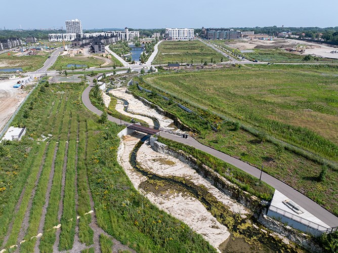 Aerial image of an urban, residential development site with an engineered bedrock channel extending through the middle on a sunny day.