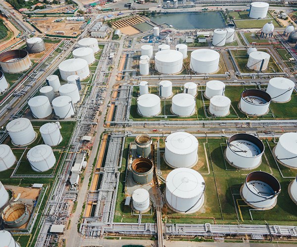 Aerial view of an industrial oil storage facility with numerous large white tanks, pipelines, and surrounding infrastructure.